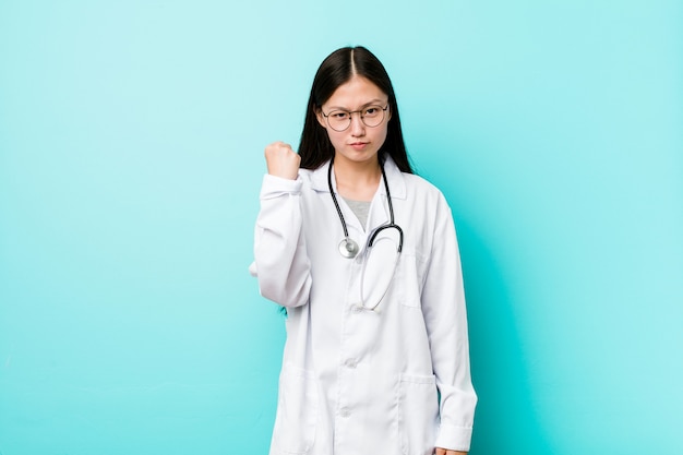 Mulher chinesa nova do doutor que mostra o punho à câmera, expressão facial agressiva.