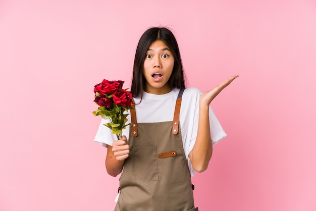 Mulher chinesa nova do jardineiro prendendo rosas isoladas surpreendidas e chocadas.