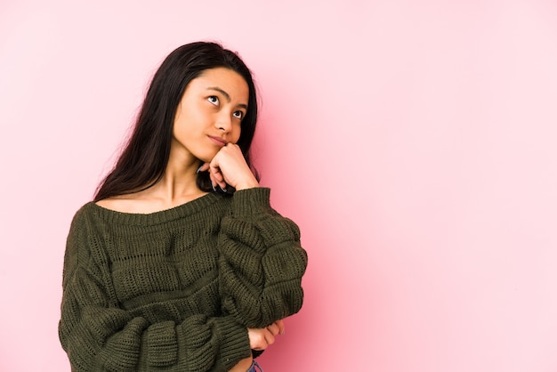 Mulher chinesa nova em uma parede cor-de-rosa que sente triste e pensativa, olhando o espaço em branco.