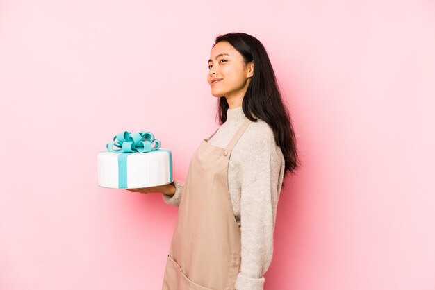 Mulher chinesa nova que guarda um bolo que olha lateralmente com expressão duvidosa e cética.