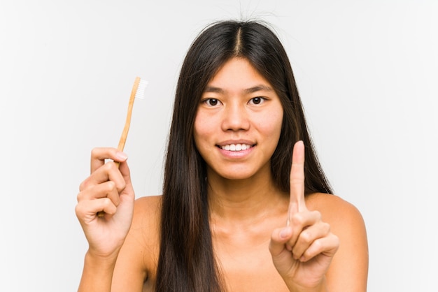 Mulher chinesa nova que prende uma escova de dentes que mostra o número um com dedo.