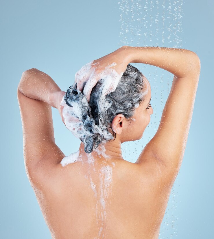 Foto mulher chuveiro e cabelo para shampoo em estúdio com costas para limpeza crescimento e caspa por fundo azul garota pessoa e modelo com gotas de água para produto sabão e espuma com bem-estar do couro cabeludo
