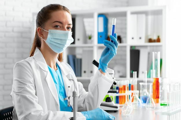 Mulher cientista ou trabalhadora de laboratório segurando um frasco de vidro com líquido químico em laboratório