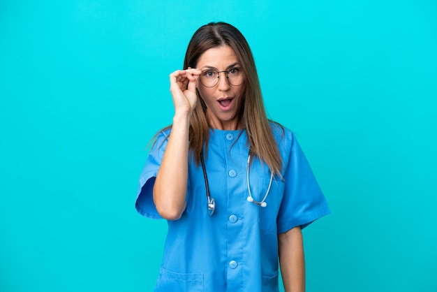 Mulher cirurgiã de meia idade isolada em fundo azul com óculos e surpresa