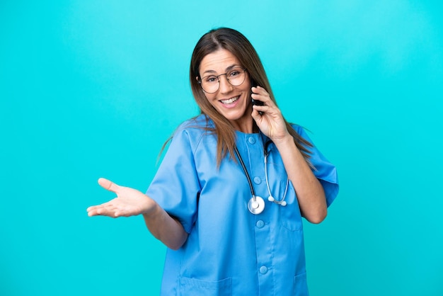Mulher cirurgiã de meia idade isolada em fundo azul, mantendo uma conversa com o celular com alguém