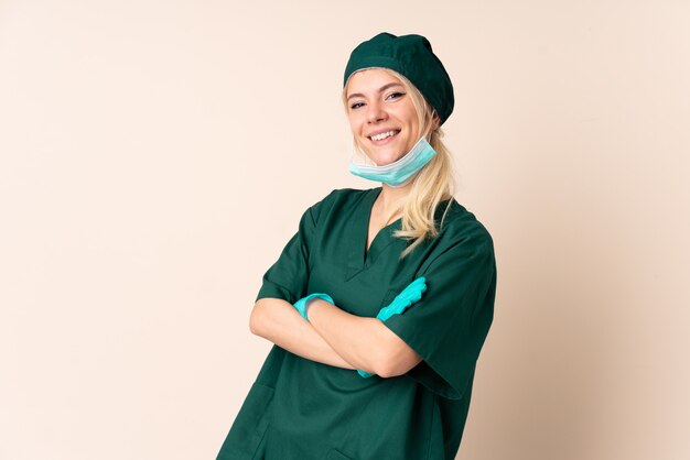 Mulher cirurgiã de uniforme verde rindo em uma parede isolada