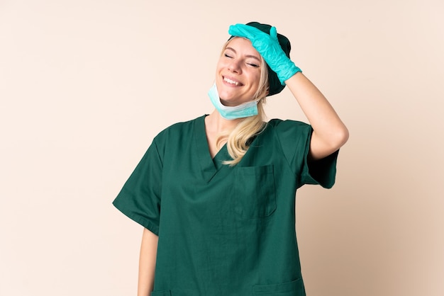 Mulher cirurgiã de uniforme verde rindo em uma parede isolada