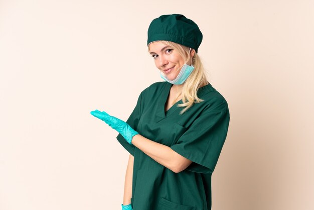 Mulher cirurgiã de uniforme verde sobre parede isolada estendendo as mãos para o lado para convidar para vir