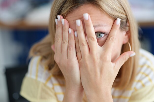 Mulher cobre o rosto com a mão olhando através dos dedos expressões faciais de emoção e sofrimento