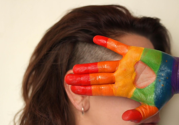 Foto mulher cobrindo o rosto com a mão pintada contra um fundo colorido