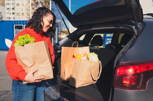 Mulher coloca pacotes na mala do carro. Compras de mantimentos.