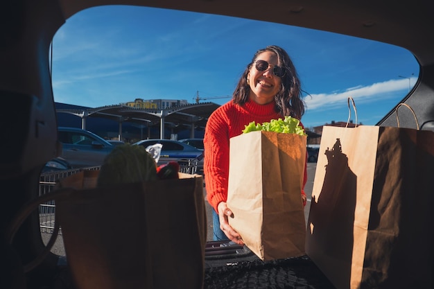 Foto mulher coloca pacotes na mala do carro para fazer compras.