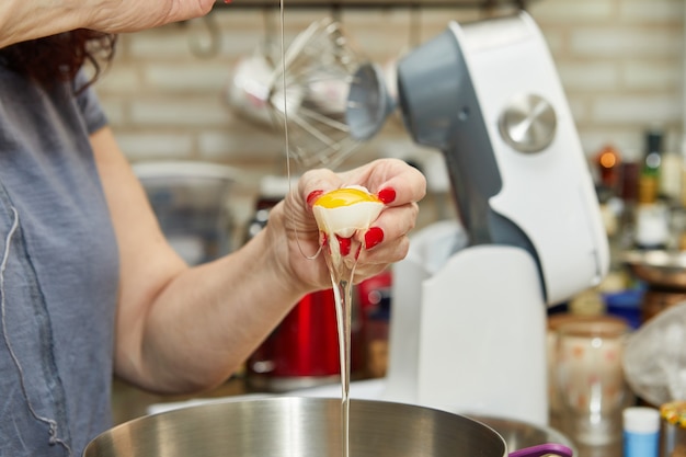 Mulher coloca um ovo na massa para fazer uma torta de queijo com raspas, uma receita passo a passo da internet.