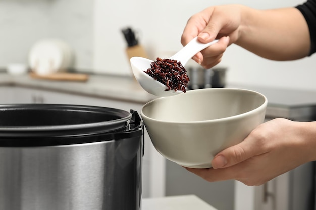 Mulher colocando arroz integral em uma tigela de fogão múltiplo na cozinha fechada