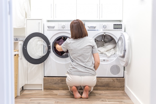 Mulher colocando as roupas na máquina de lavar roupa para lavar