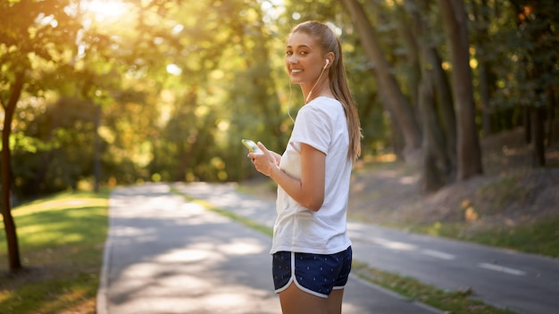 Mulher colocando fones de ouvido para ouvir música antes de correr no parque de verão