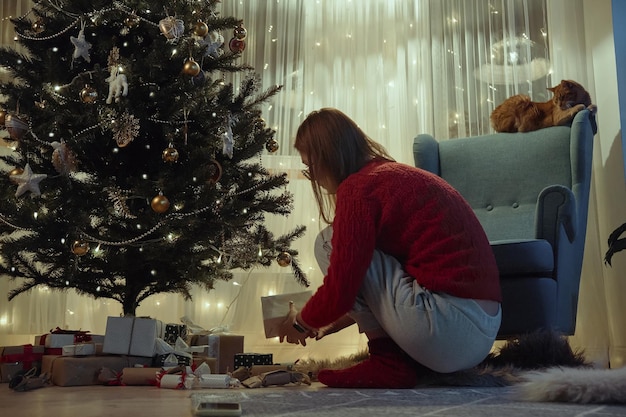 Mulher colocando presentes debaixo da árvore de Natal na véspera de Natal ou na véspera de Ano Novo à noite