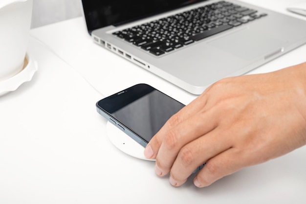 mulher colocando smartphone carregando bateria com carregador sem fio perto do computador laptop