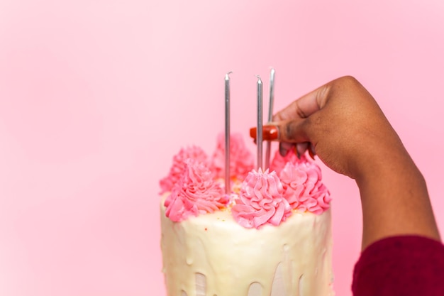 Mulher colocando velas de aniversário no bolo de creme de creme de manteiga rosa e branco com granulado rosa e gotejamento de ganache de chocolate branco.