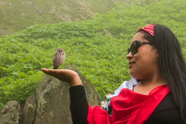 Mulher com a mão estendida fingindo segurar uma coruja no meio de uma paisagem