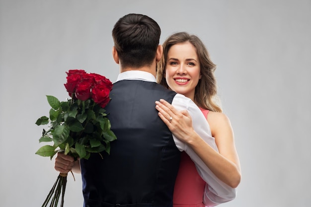 Mulher com anel de noivado e rosas abraçando homem