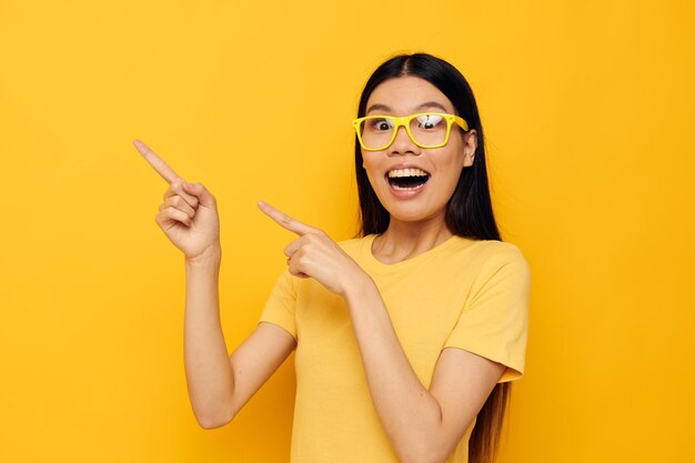 Mulher com aparência asiática em óculos gesticulando com as mãos copyspace fundo amarelo inalterado