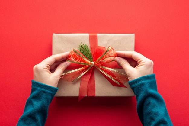 Mulher com as mãos amarrando um laço no presente de Natal no vermelho