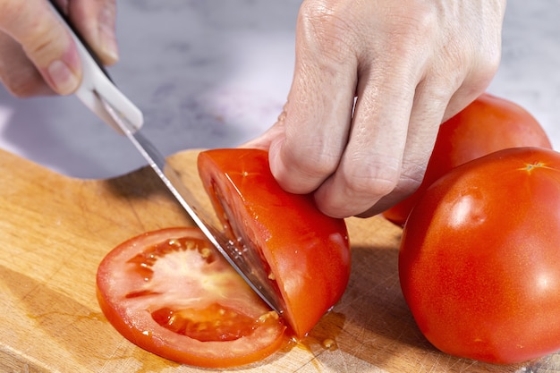 mulher com as mãos cortando fatias de tomate fresco em uma placa de madeira