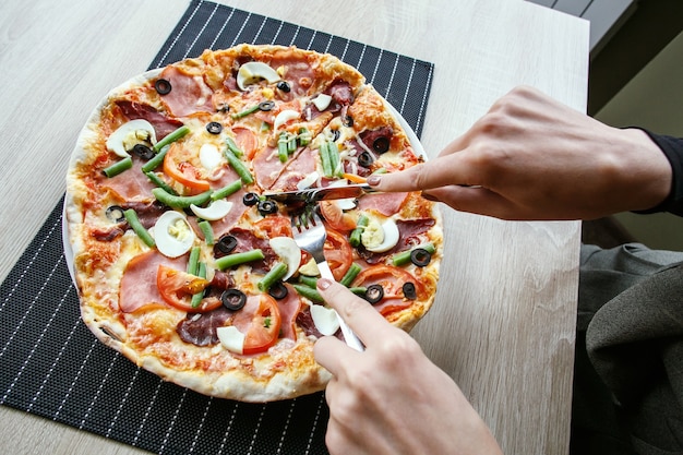 Mulher com as mãos cortando pizza fresca com feijão, queijo, presunto, ovos, calabresa e vegetais