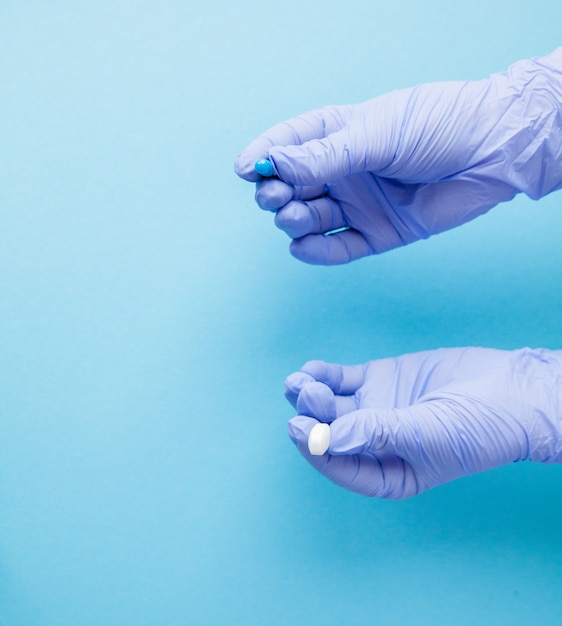 Mulher com as mãos em luvas médicas dando dois comprimidos grandes. Azul e branco