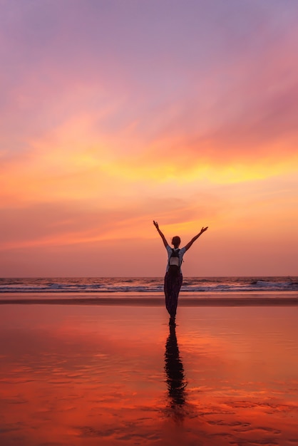 Mulher com as mãos levantadas sente liberdade e apreciando o pôr do sol de Goa