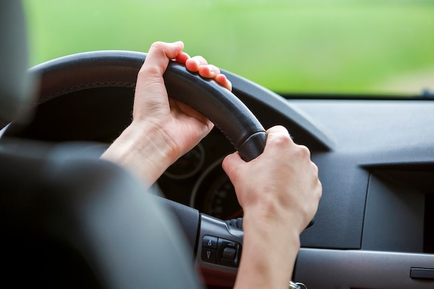 Mulher com as mãos no volante dirigindo um carro.