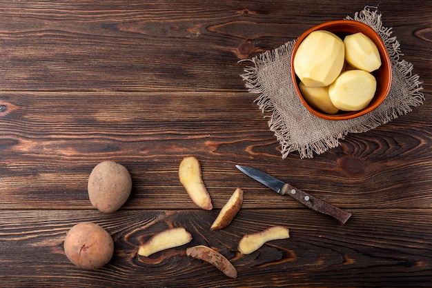 Mulher com as mãos para descascar batata. Limpe as batatas na superfície de madeira. Reparar alimentos para cozinhar.