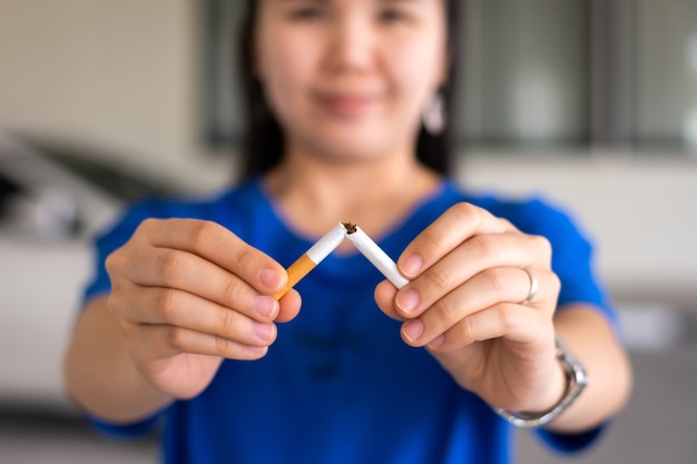 Mulher com as mãos segurando e quebrando o cigarro para parar de fumar