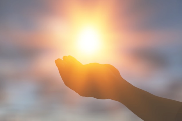 Mulher com as mãos segurando o sol ao amanhecer. Conceito de liberdade e espiritualidade.