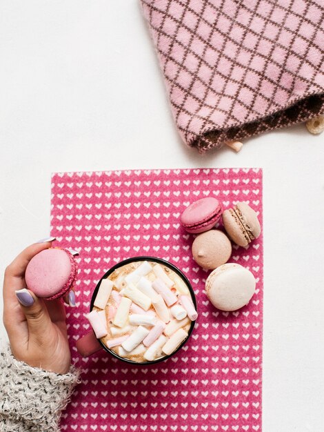 Mulher com as mãos segurando um macaroon e um cappuccino quente com marshmallow