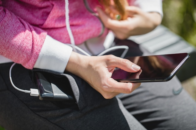 Mulher com as mãos segurando um smartphone preto carregando bateria de banco de energia externo