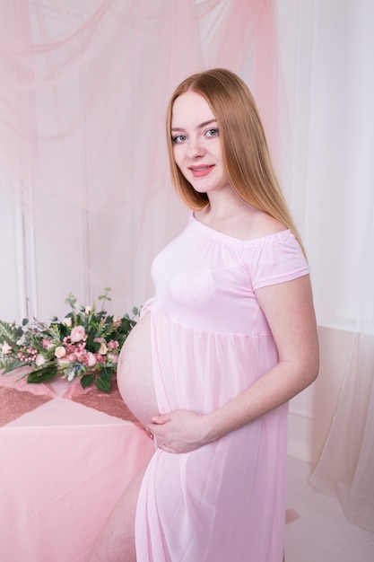 Mulher com as mãos sobre a barriga no vestido rosa com flores sobre fundo