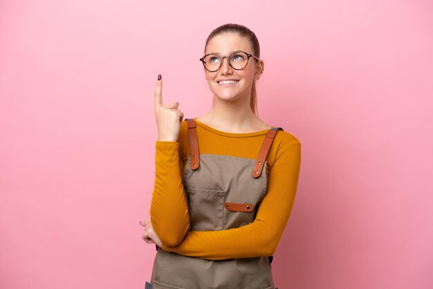 Mulher com avental isolado no fundo rosa apontando uma ótima ideia