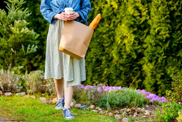 Mulher com baguete na sacola de compras e café em um jardim