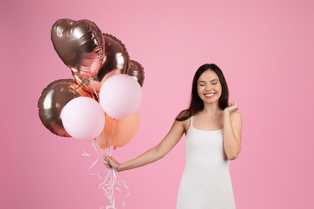 Foto mulher com balões em estado de espírito de celebração em fundo rosa