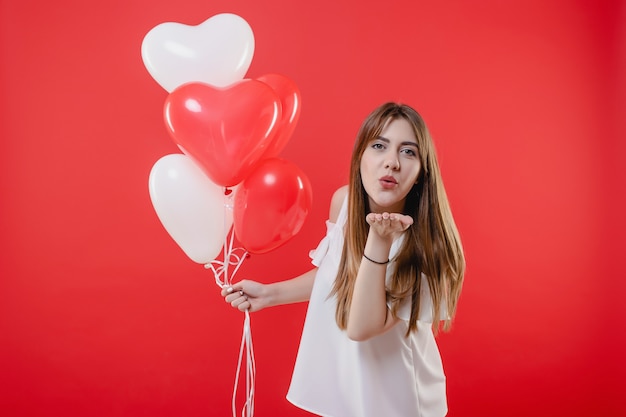 Mulher com balões em forma de coração, dando beijo beijo isolado sobre o vermelho