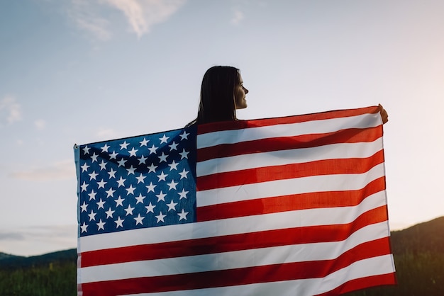 Mulher com bandeira dos estados unidos apreciando o pôr do sol