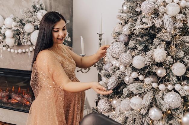 Mulher com barriga redonda com bebê dentro decorando a árvore de Natal, comemorando o feriado de Ano Novo