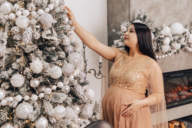 Mulher com barriga redonda com bebê dentro decorando a árvore de Natal, comemorando o feriado de ano novo.