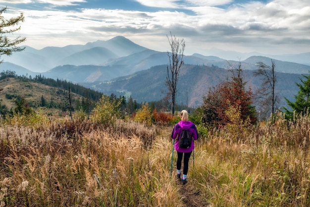 Mulher com bastões de caminhada caminhando nas montanhas de outono