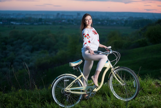 Mulher com bicicleta retro na colina à noite