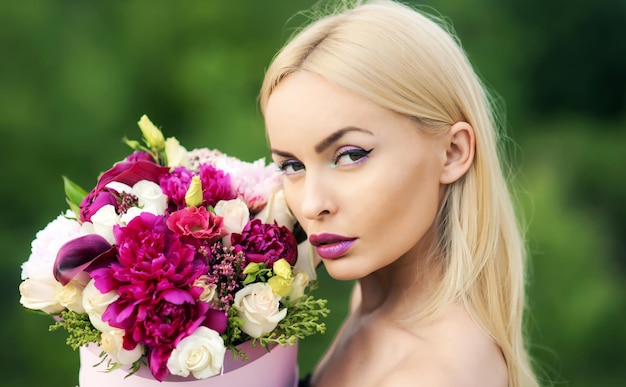 Mulher com buquê de flores, presente de menina maquiagem feminina. cabelo loiro ideal, pele perfeita.