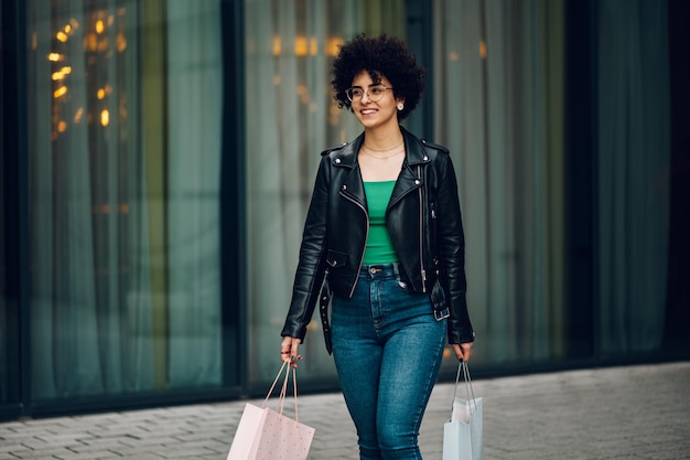 Mulher com cabelo afro segurando sacolas de compras enquanto caminhava na rua