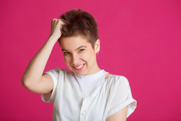 mulher com cabelo curto em uma camiseta branca em uma parede rosa com um rosto desgostoso arrancando seus cabelos